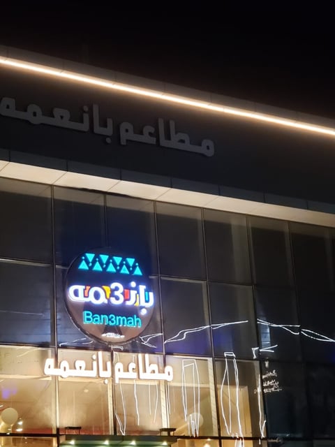 Neon sign for Banamah restaurant at night with Arabic text and illuminated storefront