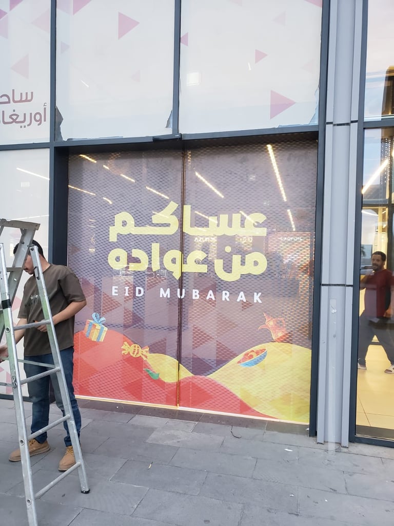 Storefront window displaying Eid Mubarak greeting in Arabic and English with festive decorations