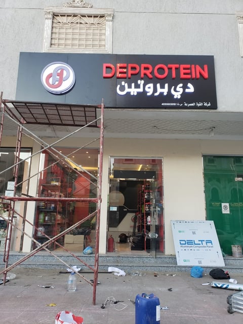 Storefront of Deprotein shop with bilingual signage, red metal door, construction scaffolding