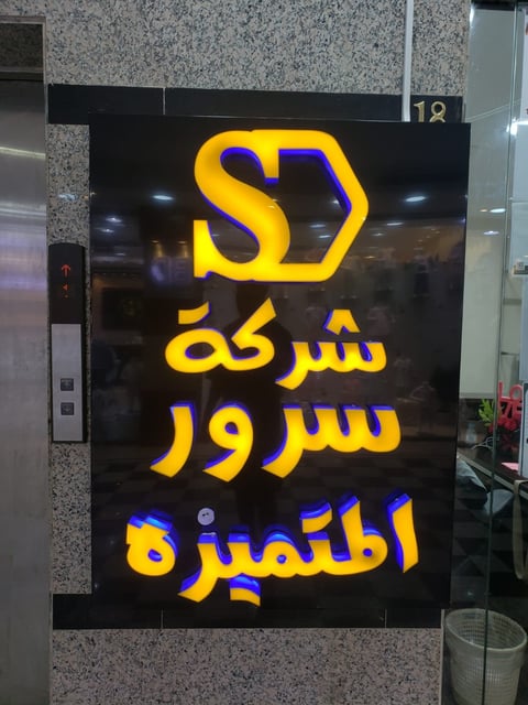 Neon sign with yellow and blue SD logo and Arabic text on black background