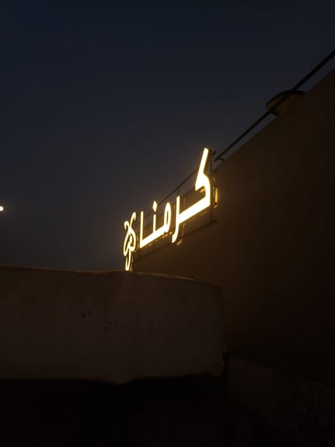 Glowing neon Arabic script sign mounted on a dark building exterior at night