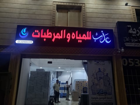 Storefront with illuminated Arabic neon sign for water and plumbing supplies shop at night