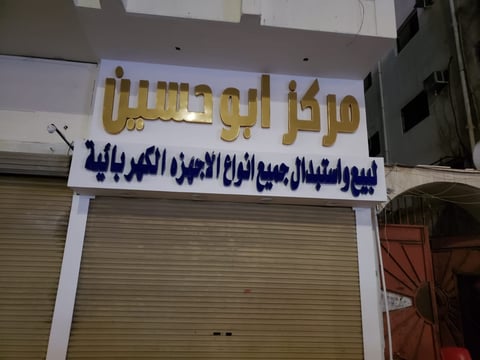 Storefront with Arabic signage in gold and blue lettering above a closed metal shutter door