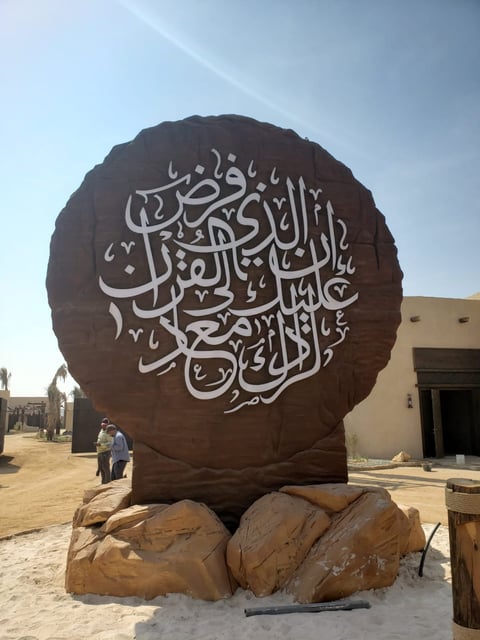 Large spherical bronze sculpture with Arabic calligraphy resting on rocky base in desert setting