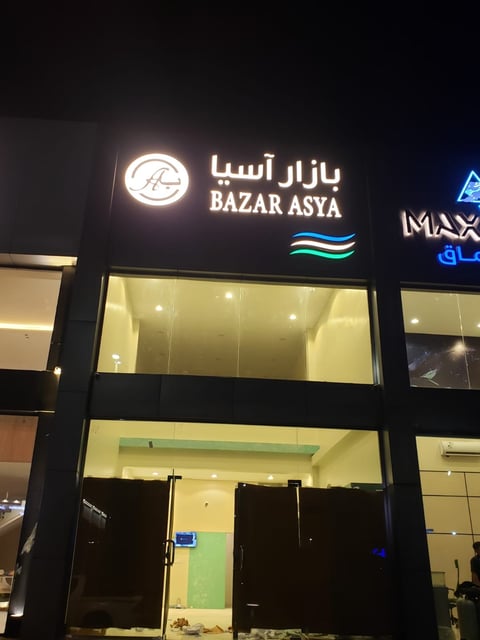 Nighttime storefront for Bazar Asya with illuminated bilingual signage in Persian and English