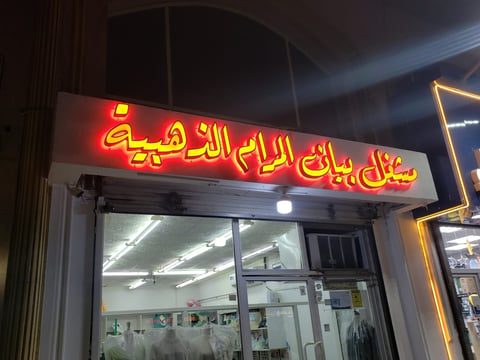 Storefront with red and yellow Arabic neon sign glowing at night, glass entrance doors and windows