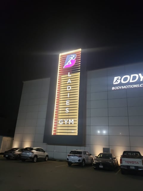 Illuminated neon sign for Ladies Gym located on building facade at night with parked cars