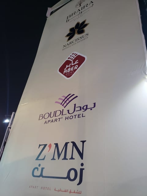 Vertical sign displaying multiple hotel and business logos including Bouldog Apart Hotel